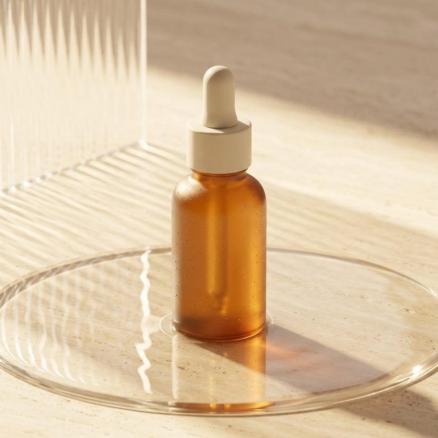 Frosted amber serum bottle with an ivory dropper standing in warm rippled light on a glass dish